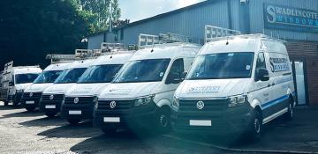 Image shows 6 white vans with livery. They are used for specialist window transportation and installation with Swadlincote Windows